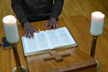 Above angle of hands of black man standing by wooden pulpit with cross on the front part between...