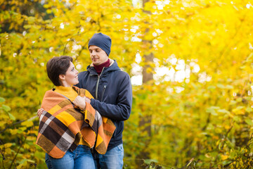 portrait of a romantic couple in autumn city park, man and woman posing among yellow leaves, woman are covered with a warm shawl