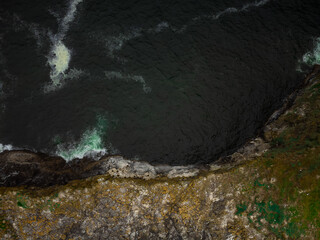 Top view of the dark surface of the ocean with light white waves running on a stone shore covered with moss. Minimalism. Abstraction. Geology, environmental protection, topography.