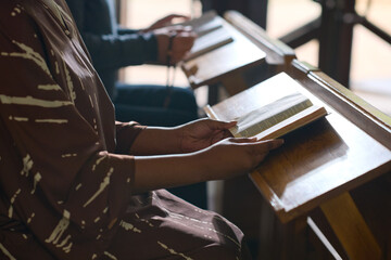 Young black woman sitting by wooden desk in Catholic or evangelical church and studying Holy Bible on seminary course