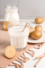 A glass with potato milk on the table with the potato tubers. Vegan trend in healthy eating. Alternative plant milk