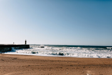 Sunny day on the ocean. Wide sandy beach with ocean waves and lighthouse. Portugal ocean. Spring day. Atlantic ocean