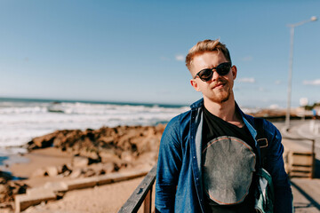 Emotional stylish blond guy posing at sea beach with happy emotions. Outdoor portrait of smiling european man enjoying ocean view