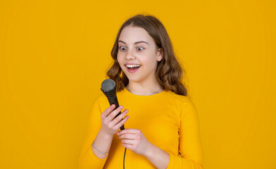 amazed teen girl with microphone on yellow background