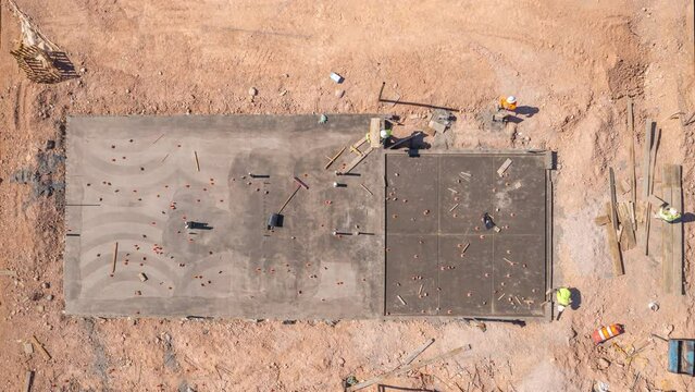 Aerial long shot of construction workers building concrete foundation of house