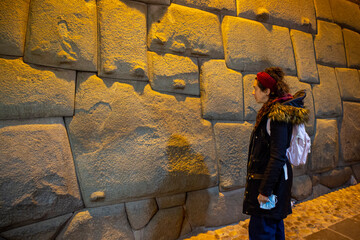 Tourist woman looking at the stone of the 12 angles at night in Cusco, Peru