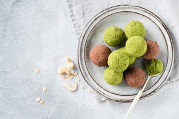 Healthy vegan raw truffles with green matcha tea and cocoa on plate, top view grey concrete background
