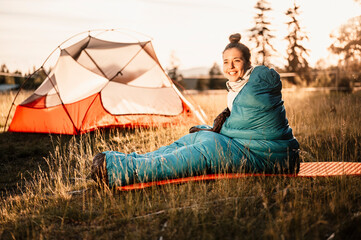 Woman relaxing and lie in a sleeping bag in the tent. Sunset camping in forest. Mountains landscape...