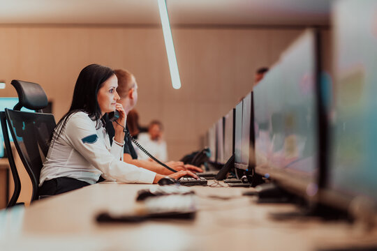 Female security guard operator talking on the phone while working at workstation with multiple displays Security guards working on multiple monitors