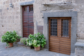 Exterior shot of ancient, arched wooden door of an old stone building with flower pots beside doors. Cobblestone courtyard in  front of the building.