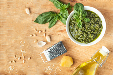 Ingredients for pesto sauce in the white bowl. Green basil leaves, Parmesan cheese and pine nuts on the wooden background. Flat lay. Overhead view