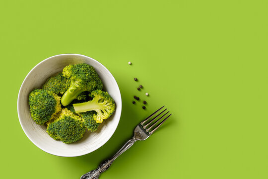 Fresh raw broccoli florets in a bowl and fork over yellow green colored background. Antioxidant low calorie dieting concept. Vegetarian food recipe. Cooking vegetables. Copy space.