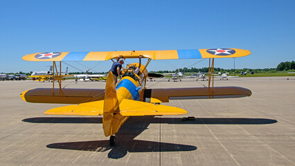 The pilot of a biplane climbs aboard to prepare for takeoff at an airshow.