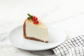 The piece of Classic New York cheesecake in the white plate decorated with red currant berries on the white background