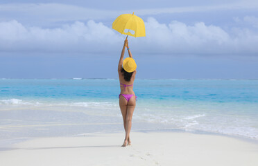 Fototapeta na wymiar girl in a bikini with a yellow umbrella on the sea sand