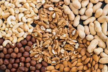 Mixed nuts on black stone table. Almonds, walnuts, cashew, hazelnut, peanut. Top view nut photo.