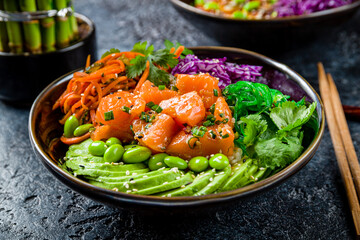 Poke with salmon, avocado, chukka, cabbage and carrot on black plate on dark stone table