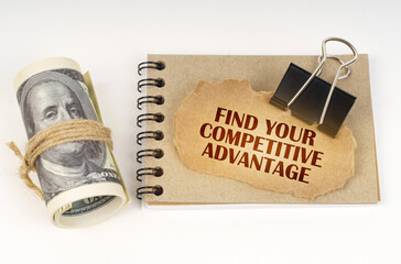 On a white surface are twisted dollars, a cardboard sign with the inscription - Find Your Competitive Advantage