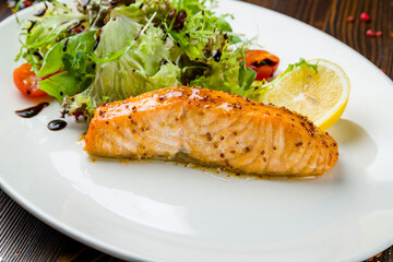 Salmon steak on the grill with greens on plate on wooden table