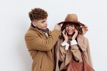 a close horizontal photo of a happy couple in stylish autumn clothes, a woman stands holding a bag in her hand, and a man adjusts her hat