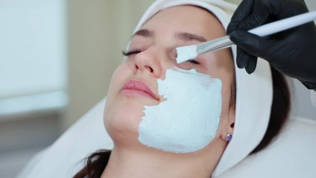 Beautician applying clay facial mask at beauty shop