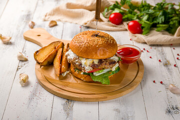 Burger with meat and cheese with potato wedges and ketchup on white wooden table