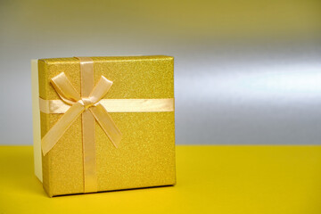 Golden gift box is tied with ribbon with bow silver background.