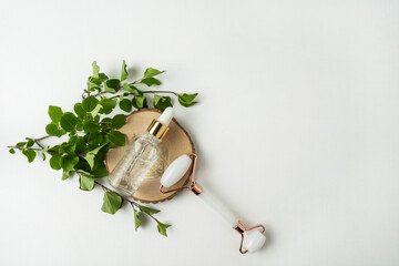 Natural antiaging face serum or essential oil lying on a wooden plate and a face roller nearby