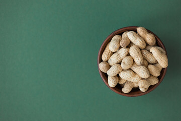 Fresh organic peanuts in the bowl on green background