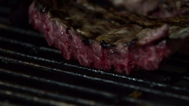 Close-up video of a delicious pork rib being cooked on a barbecue grill with charcoal embers