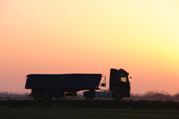 Fototapeta premium Semi-truck with tipping cargo trailer transporting sand from quarry driving on highway hauling goods in evening. Delivery transportation and logistics concept