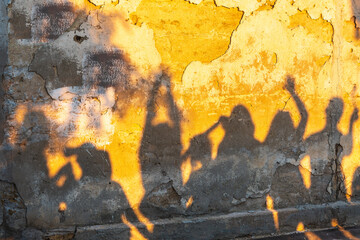 Shadows of dancing people on an old stone wall at sunset time.