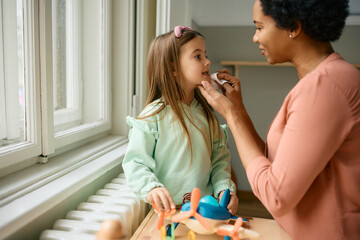 Caring black nanny wiping face little girl's face with napkin.