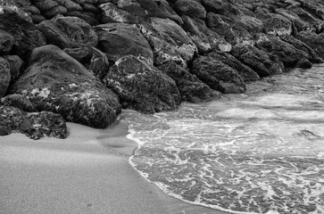 Black Rock Break Wall with an Ocean  Wave on a Sand Beach.