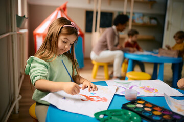 Fototapeta premium Creative little girl using watercolor paints during art class at kindergarten.