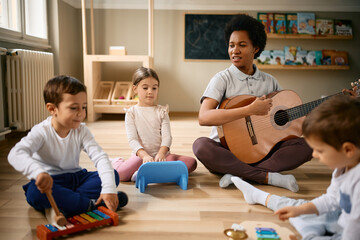 Group of children and their black female teacher playing musical instruments at preschool.
