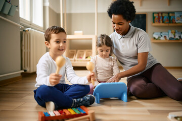 Small kids and their black female teacher enjoy in playing music at kindergarten.