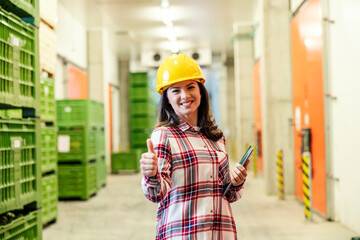 Portrait of a female manager in factory holding a tablet, giving thumbs up and smiling at the camera.