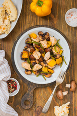 Chicken stew with mushrooms, sweet peppers and garlic arrows in a gray plate on a wooden background.