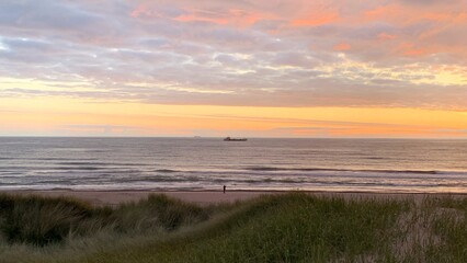 ship at sea seen from a lonely person beach in the evening, sunset, logistics, economy, shipping, ocean freight, transport, shipping company