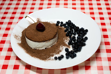 Ice cream sprinkled with chocolate with cherries and blueberries on a white plate.