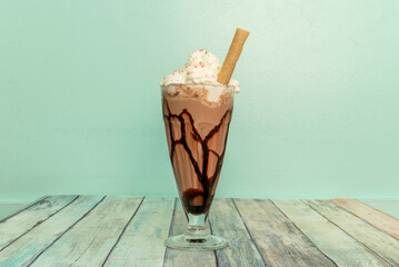 Delicious chocolate milkshake with syrup, whipped cream and a cookie straw in a glass jar