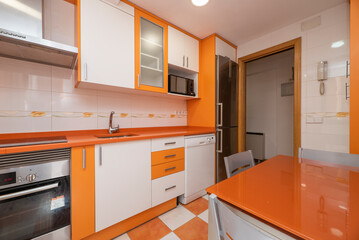 Kitchen with bright orange and white cabinets, the same tiled floor and matching table