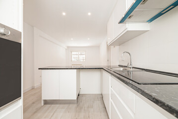 Open plan kitchen with white cabinets with doors and drawers and black countertops in a room with a light wood floor and plain white painted walls