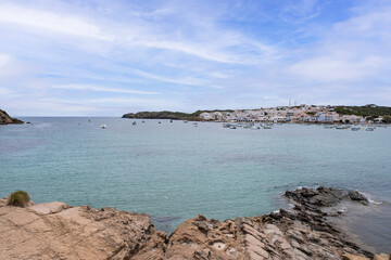 Mediterranean fishing village with white houses in a turquoise water bay, with sport boats on the water on a sunny day, Es Graus, Menorca, Balearic Islands, Spain