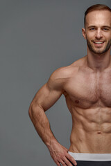Fototapeta premium Croped shot of Young male athlete posing. Handsome athletic male power guy. Fitness muscular person. Young athlete showing muscles in the studio, posing shirtless on gray background.