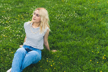 Fototapeta premium blond Caucasian girl resting on the green grass and looking up. medium full shot. High quality photo