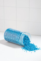 Package of blue shiny crystal salt on the background of the bathroom wall. Jar with scattered...