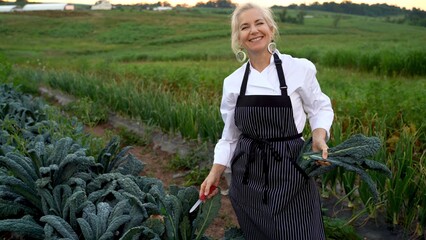 Portrait of smiling blonde, female chef picking fresh kale for a farm to table restaurant.