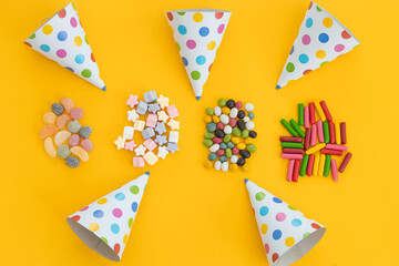 many different candies, sweets and birthday hat on yellow background